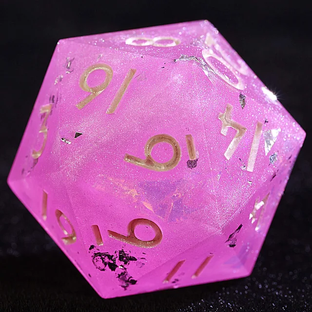Close-up of a pink, glittering polyhedral die with metallic numerals and silver foil flecks.