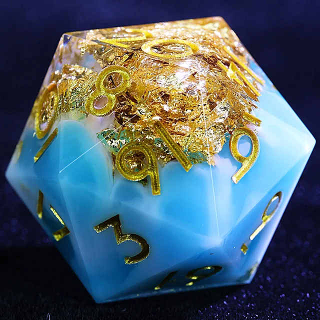 Close-up of a blue and pearly white D20 with gold-toned foil and gold numbers.