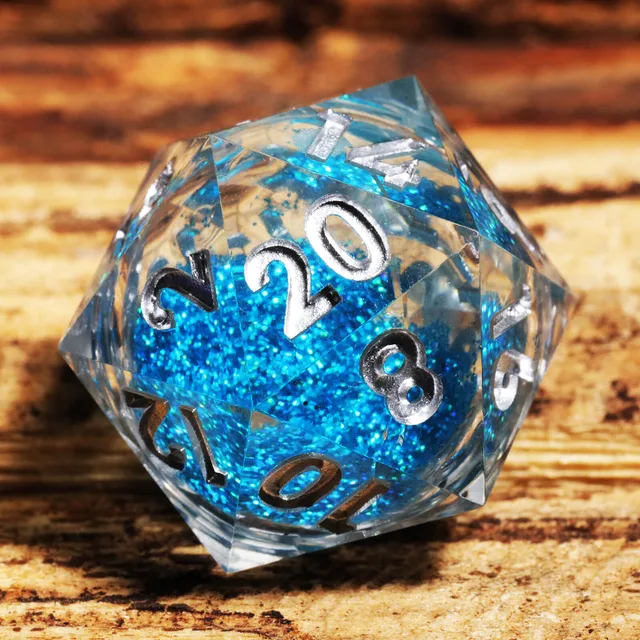 Close-up of a clear D20 with blue glitter core and silver numbers on wood.