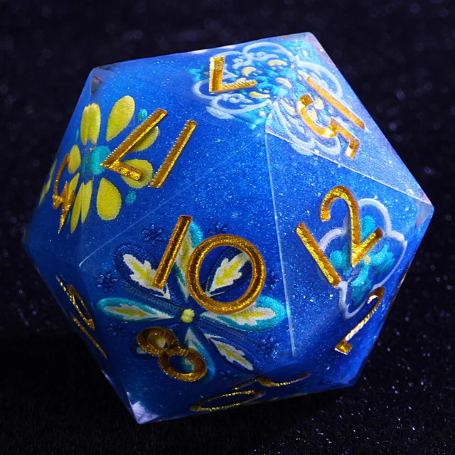 Close-up of a blue glitter D20 with gold numbers and turquoise, yellow and white floral designs.