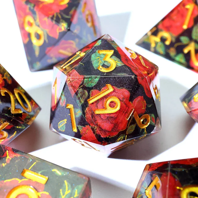 Close-up of a red flower and black D20 with gold-coloured numbers.