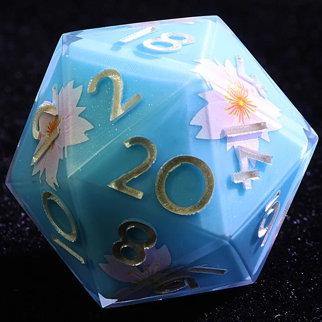 Close-up of a blue D20 with pale pink flowers and gold numbers.