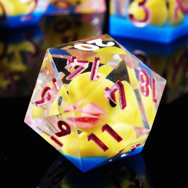 Close-up of a transparent D20 with a yellow duck and pink numerals.