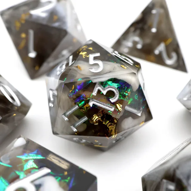 Close-up of a smoky D20 with iridescent green-blue accents, gold flecks and silver numbers.