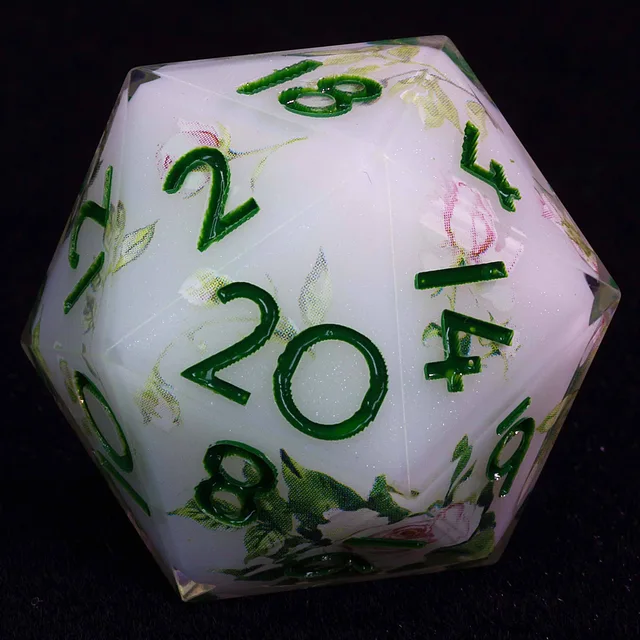 Close-up of an ivory-white D20 with green numbers and pink floral detailing.