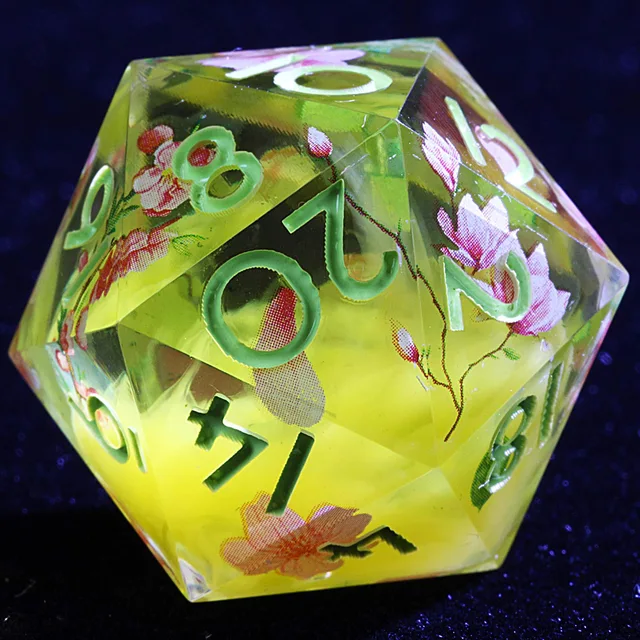 Close-up of a golden-yellow and clear D20 with pink blossoms and pale green numbers.