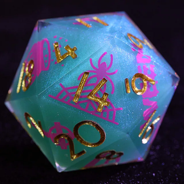 Close-up of a blue-green glitter D20 with gold numbers and a pink spider and web design.