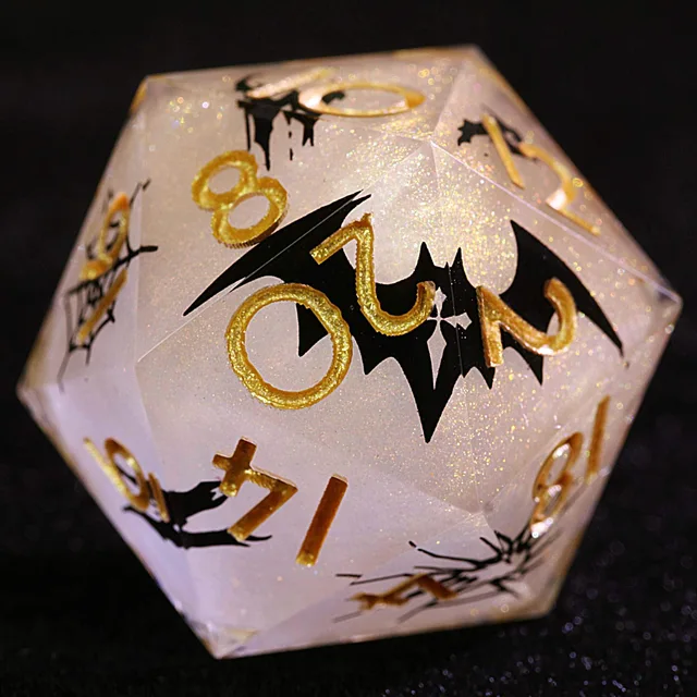 Close-up of a translucent glittering D20 with gold numbers and a black bat silhouette.