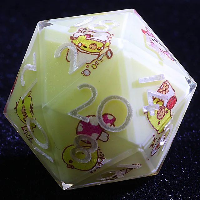 Close-up of a pale yellow D20 with silvery-white numbers and colourful chick and food illustrations.