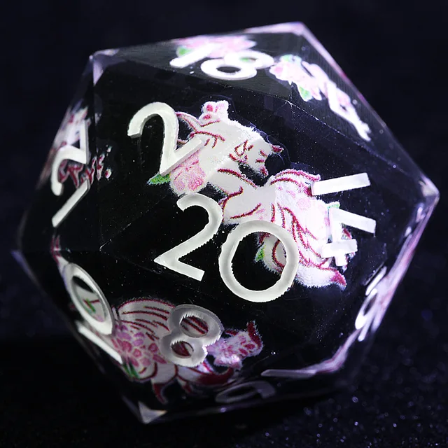 Close-up of a black polyhedral die with white numbers and a pink-and-white illustrated figure.