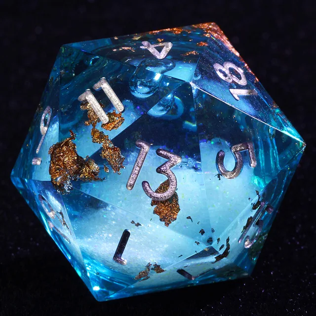 Close-up of a transparent blue D20 with a pale centre, copper-gold flecks and silver-coloured numbers.