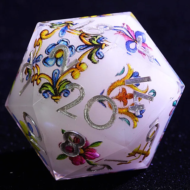 Close-up of a pale white D20 with colourful floral scrollwork and silver numbers.