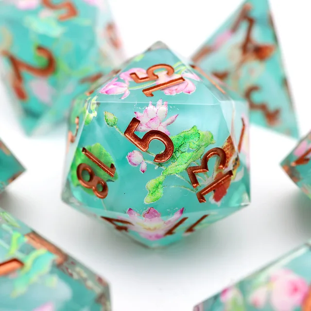 Close-up of a turquoise D20 with lotus flowers, green leaves and copper-coloured numbers.