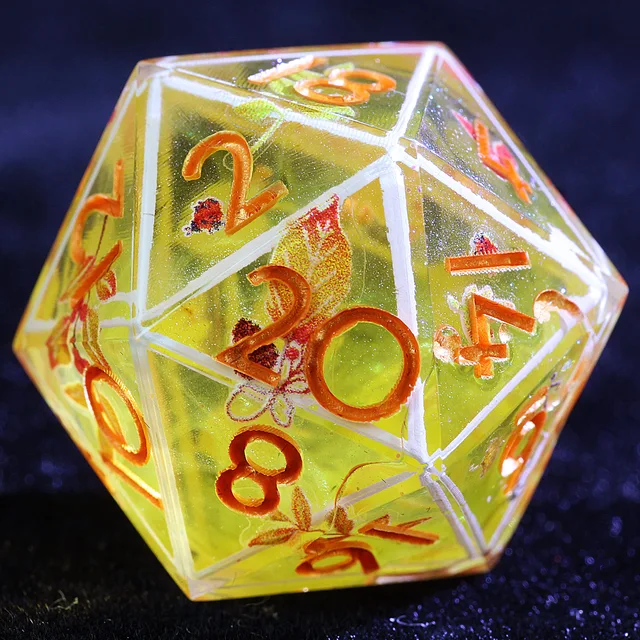 Close-up of a translucent golden-yellow D20 with orange numbers, white edge lines, and autumn motifs.