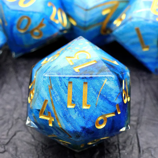 Close-up of a blue swirling D20 with gold numbers on a dark surface.