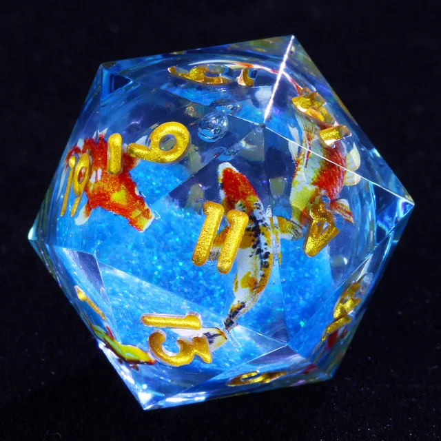 Close-up of clear blue D20 with gold numbers and red, orange and white fish imagery.