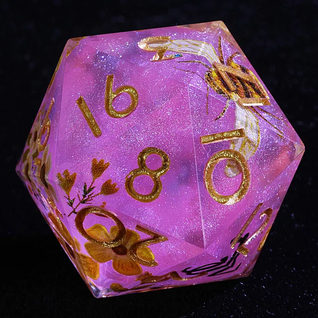 Close-up of a pink glitter die with gold numbers, a bee and flowers.