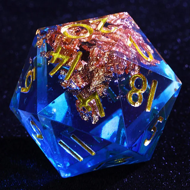 Close-up of a translucent blue D20 with gold numbers and copper-gold flakes.