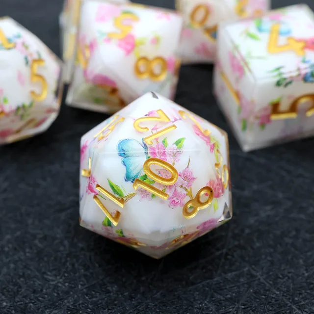Flower-and-butterfly D20 with gold numbers on a black surface.