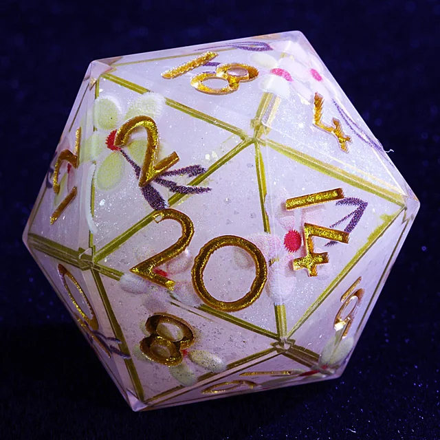 Close-up of a pale floral D20 with gold numbers and face borders.