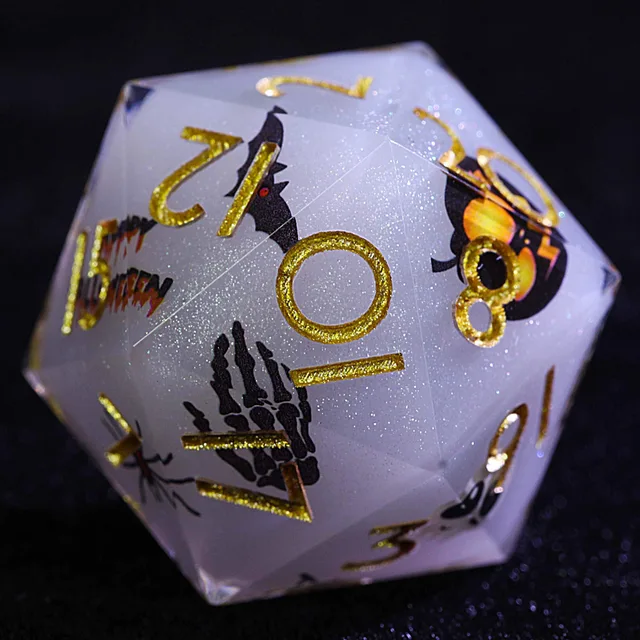 Close-up of a pale gray-lavender glitter D20 with gold numbers, a bat, skeletal hand and pumpkin design.