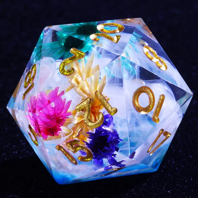 Close-up of a translucent blue and white D20 with colourful flower inclusions and gold numbers.