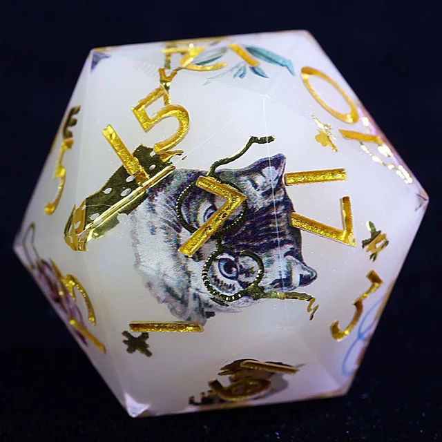 Close-up of a pearl-white D20 with gold numbers and a grey-blue cat illustration.