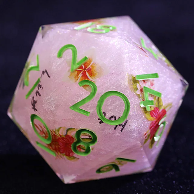 Close-up of a pale pink sparkly D20 with green numerals and floral designs.