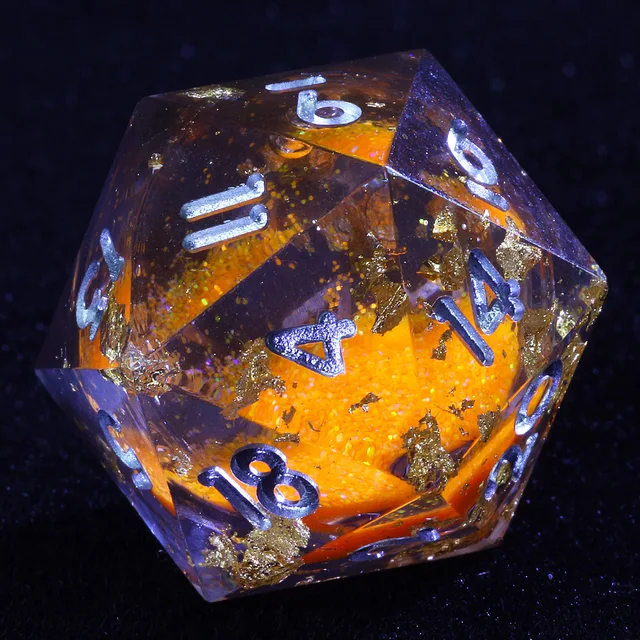 Close-up of a clear D20 with an orange glitter core, gold-coloured flecks and silver-coloured numbers.