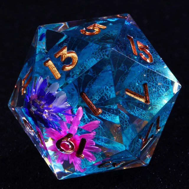 Close-up of a clear D20 with blue lace-like inclusions, pink and purple flowers, and copper-gold numbers.