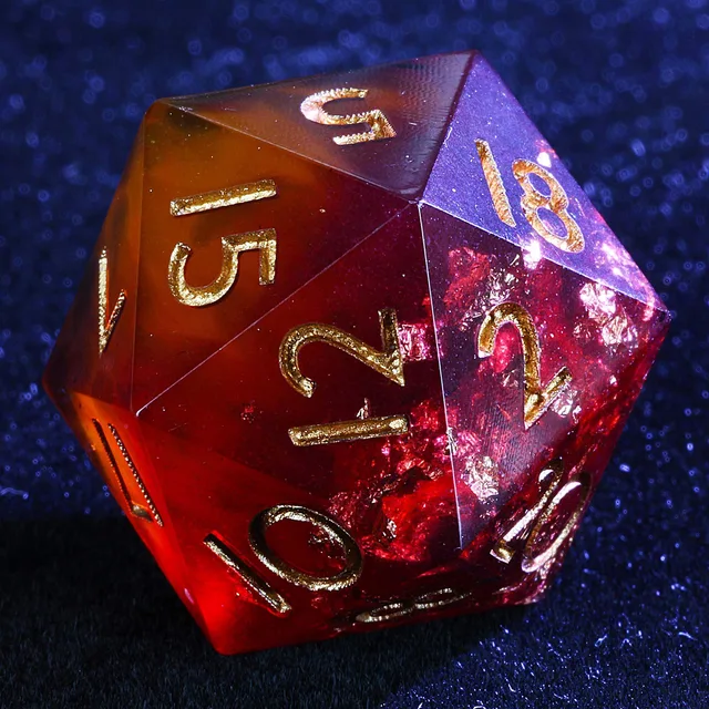 Close-up of a translucent crimson and amber D20 with gold-coloured numbers and reflective flecks.