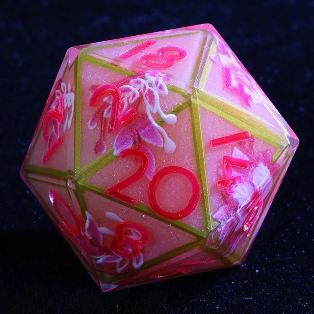Close-up of a pink floral D20 with bright pink numbers and gold-toned edge lines.