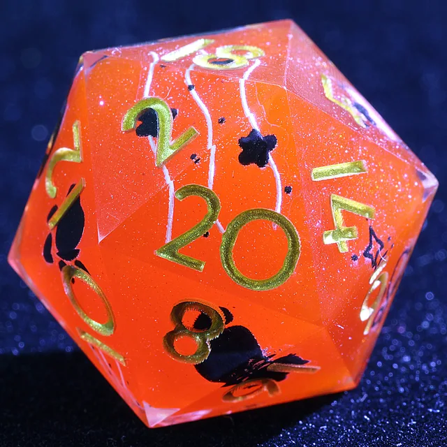 Close-up of a crimson-orange glitter D20 with gold numbers and black decorative motifs.