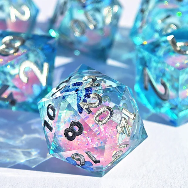 Close-up of an aqua-blue D20 with a pink core, blue butterfly shapes, and silver-toned numerals.