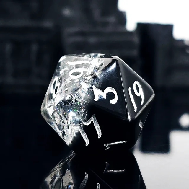 Seven resin polyhedral dice with blended black and transparent areas, reflective silver flecks and white numerals.