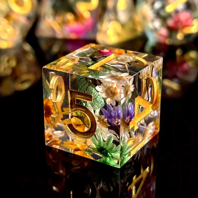 Clear, sharp-edged polyhedral dice with gold-coloured numbers, green-veined leaves and small multicoloured flowers.