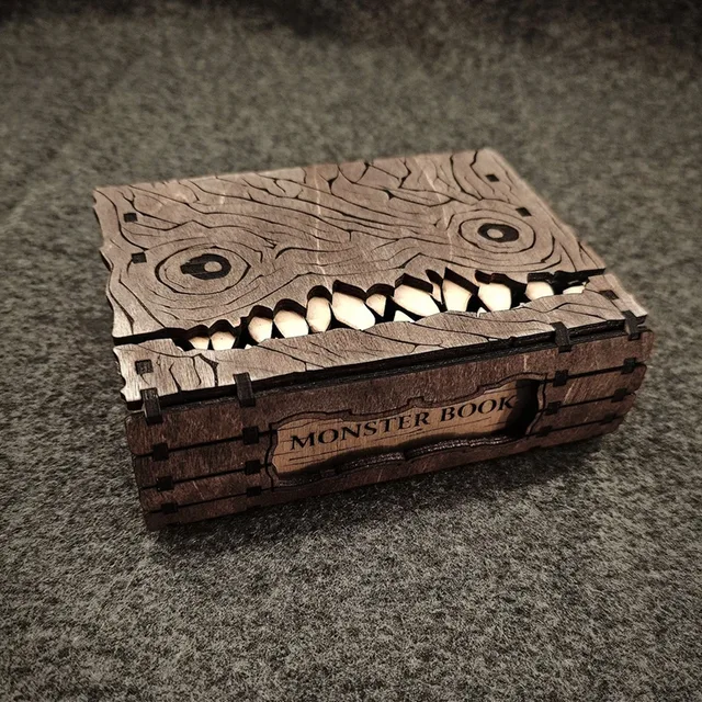 Brown book-shaped wooden storage box with dark monster-face lines, circular eyes, pointed teeth and a recessed side label panel.