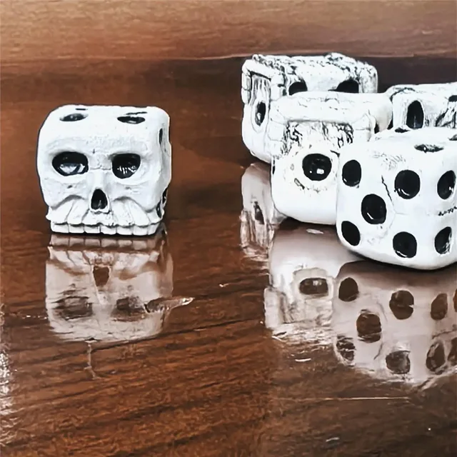White skull-shaped six-sided dice with black pips, dark eye sockets, sculpted teeth and fine crack-like markings.
