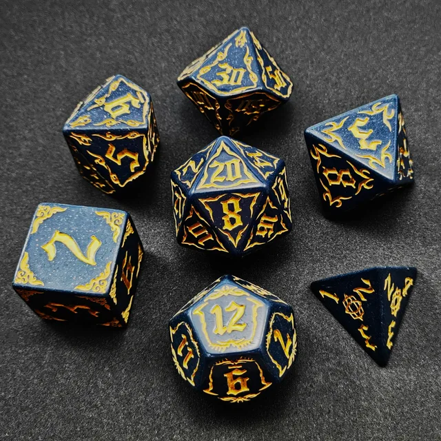 Dark blue speckled polyhedral dice with yellow-gold numbers and flame-like borders beside a black bag with a gold dragon graphic.